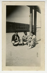 Three men sitting outside with building in the backgroud